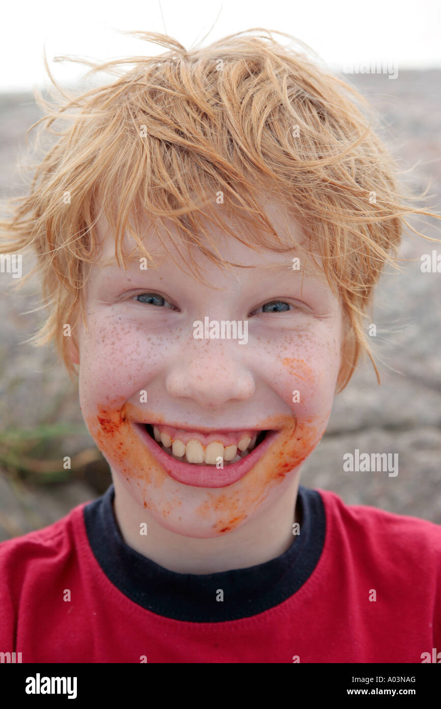 Portrait of a young red haired boy with freckles and a very dirty face smiling into the camera. Stock Photo