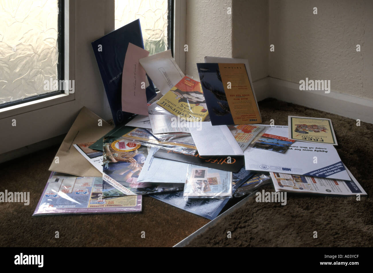 Junk mail envelopes from letter box piled up against inside of glazed entrance doorway & door mat domestic residence below letter box Essex England UK Stock Photo