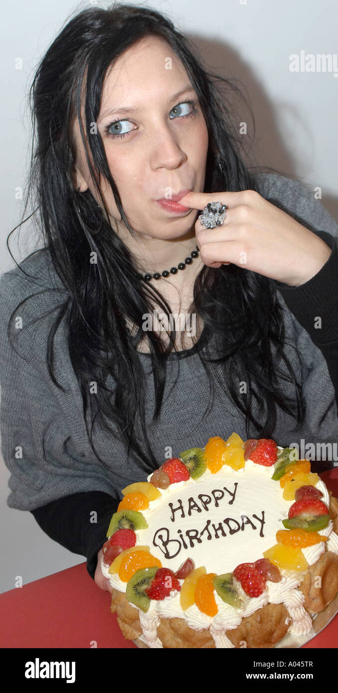 Young woman tasting a birthday cake licking her fingers Stock Photo