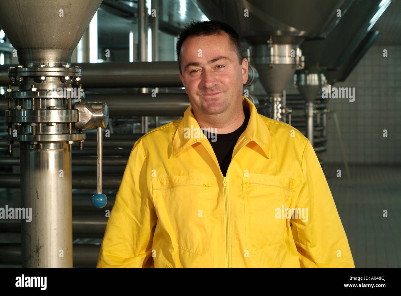 Male Brewery Worker Standing by Industrial Brewing Equipment Stock Photo
