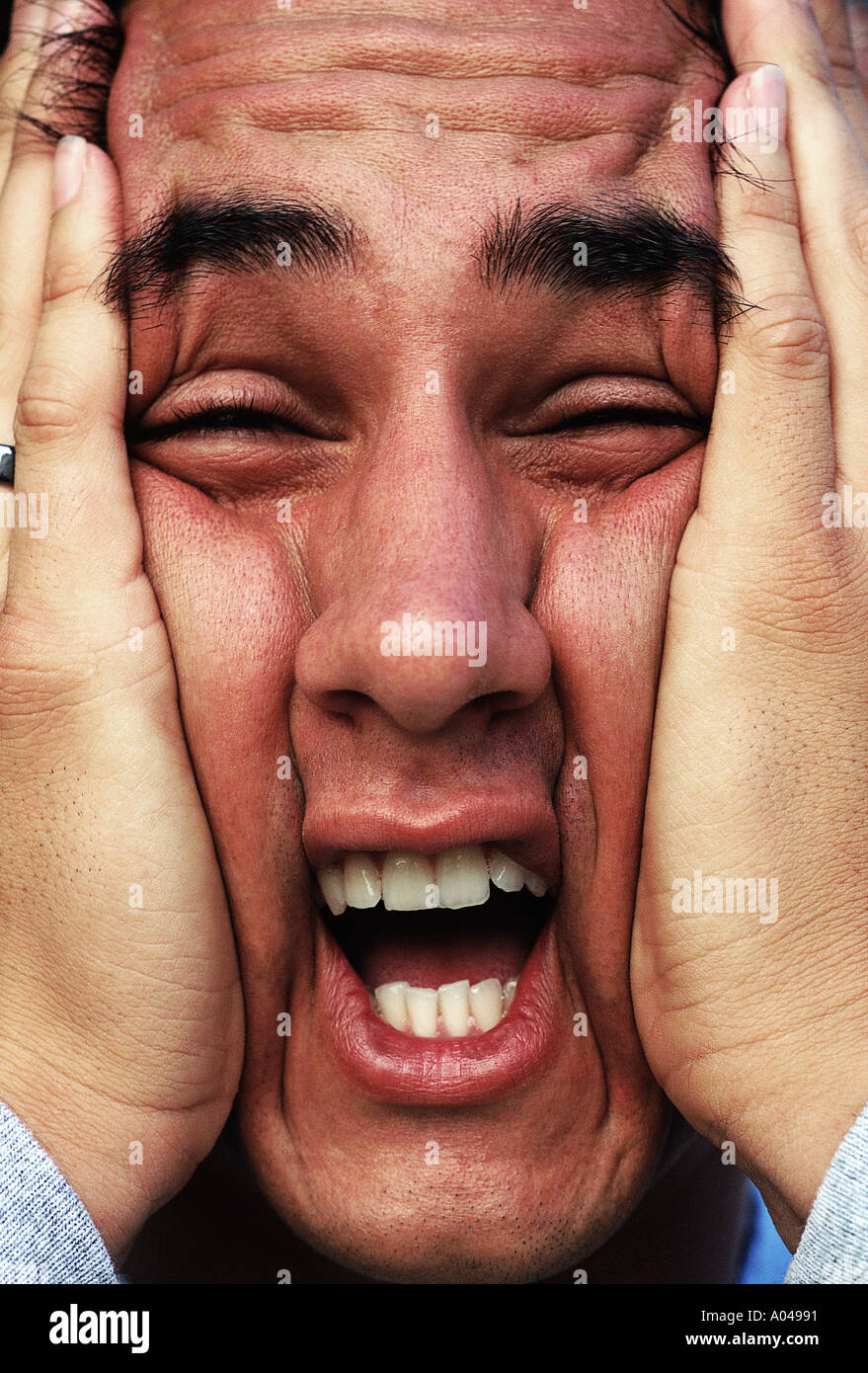 Portrait of a young man squeezing his face together with his hands Portrait of a young man squeezing his face together with his hands