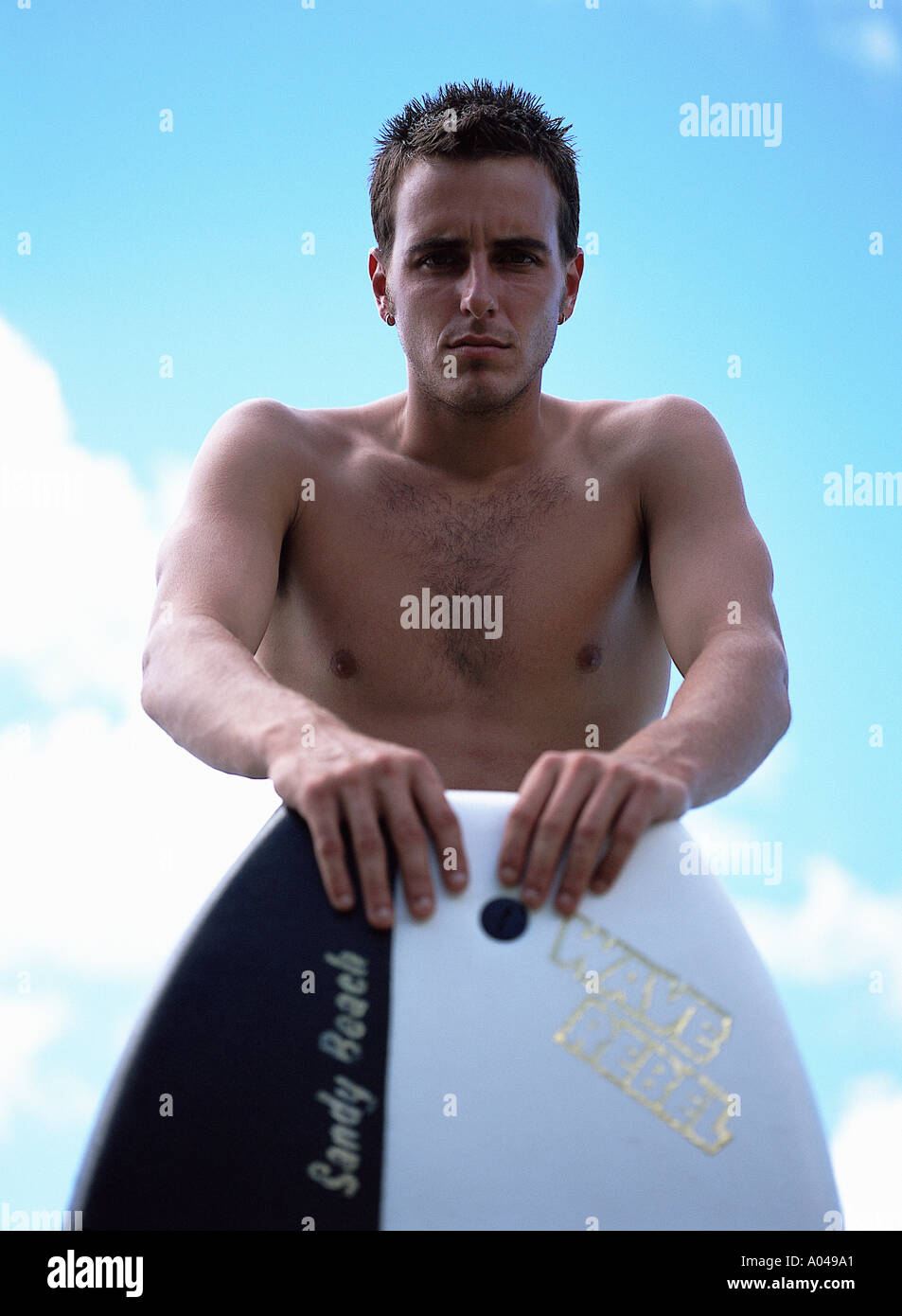 Portrait of a young man standing behind a surfboard  looking at the camera Stock Photo