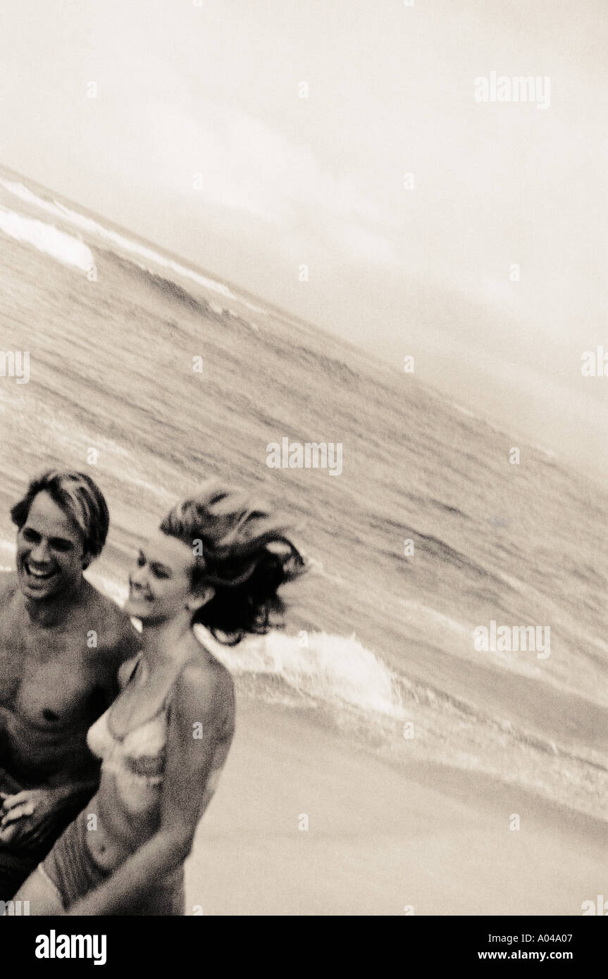 Young couple holding hands running along the beach Stock Photo