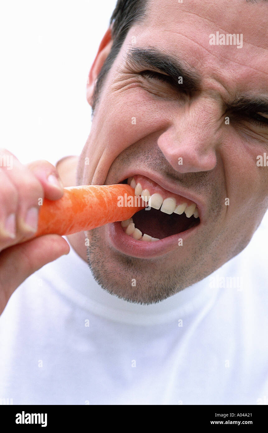 Portrait of a young man eating a carrot Stock Photo