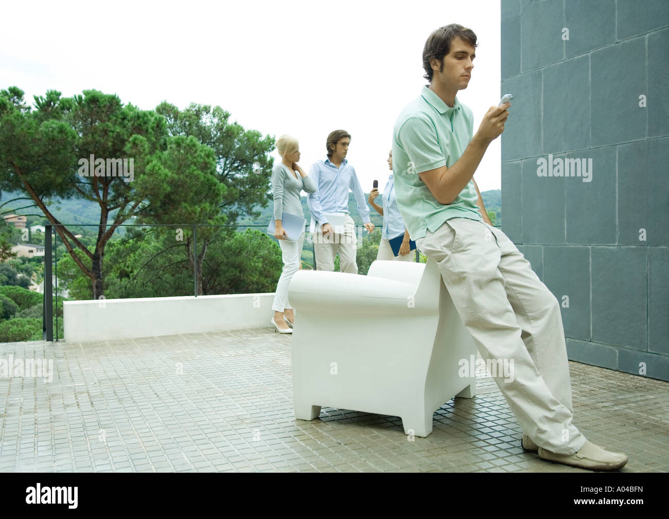 Casually dressed young executives working outdoors, man in foreground checking cell phone messages Stock Photo