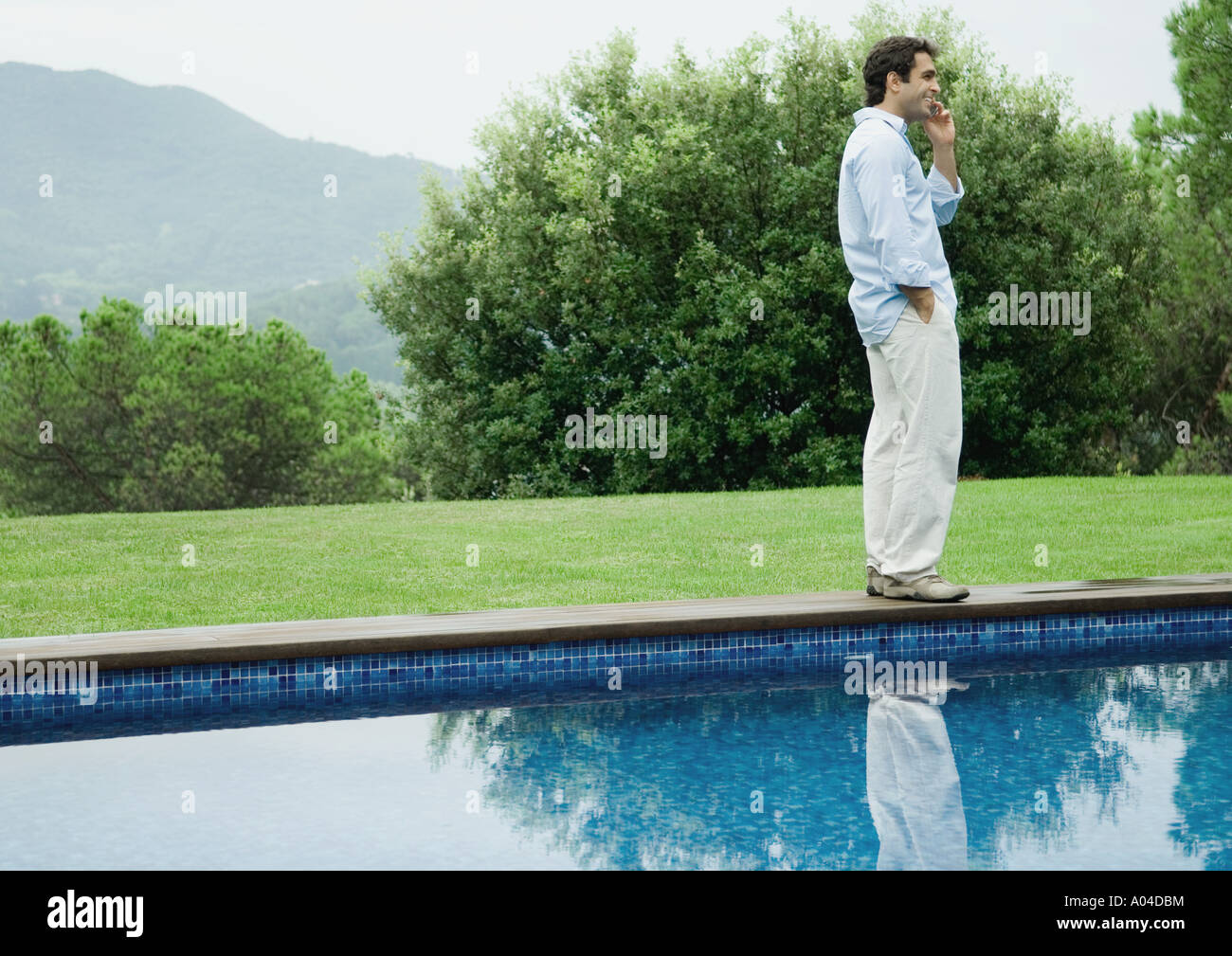 Man using cell phone by edge of pool Stock Photo