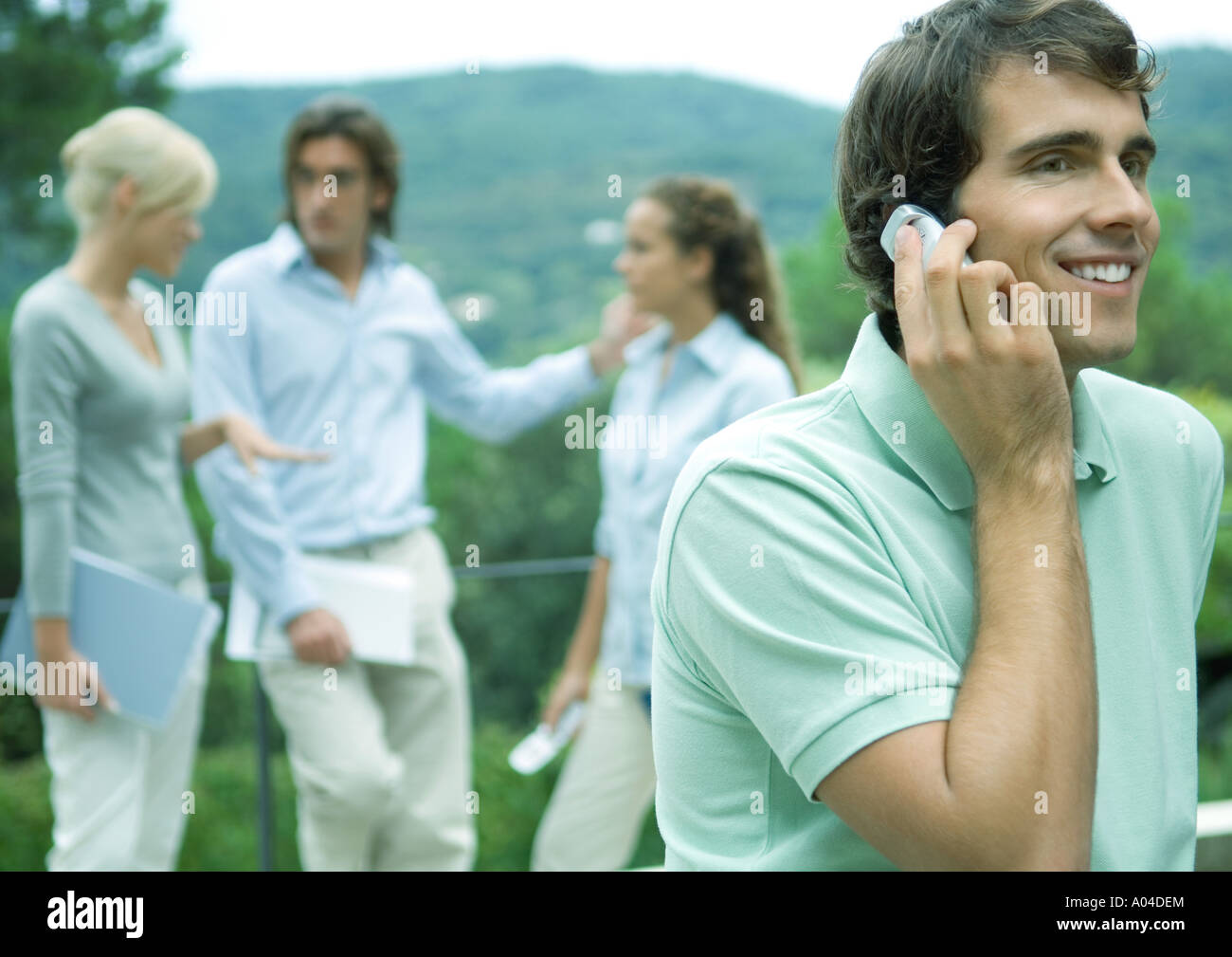 Casually dressed young executives working outdoors, man using cell phone in foreground Stock Photo