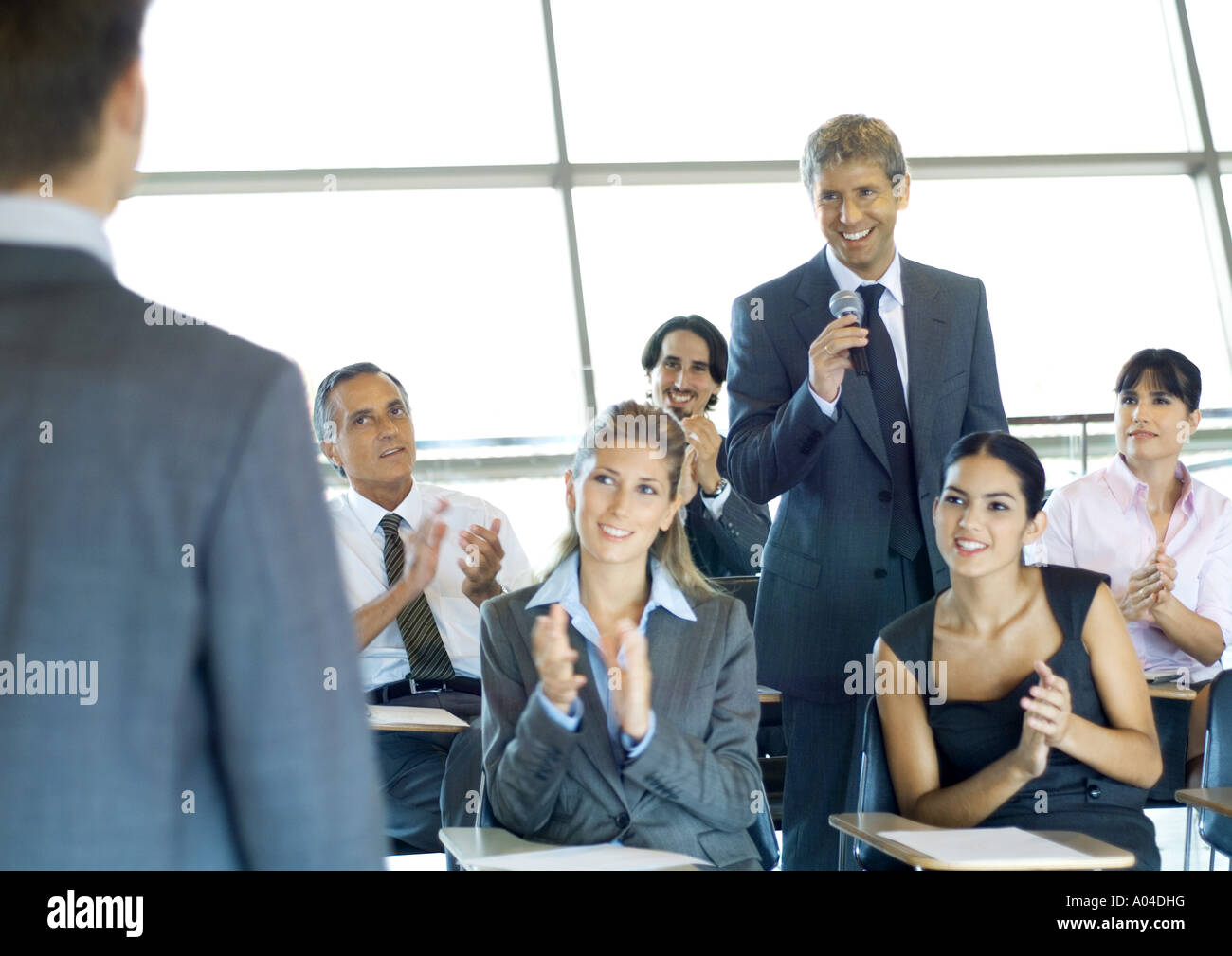 Executives in seminar, one man holding microphone, others clapping Stock Photo