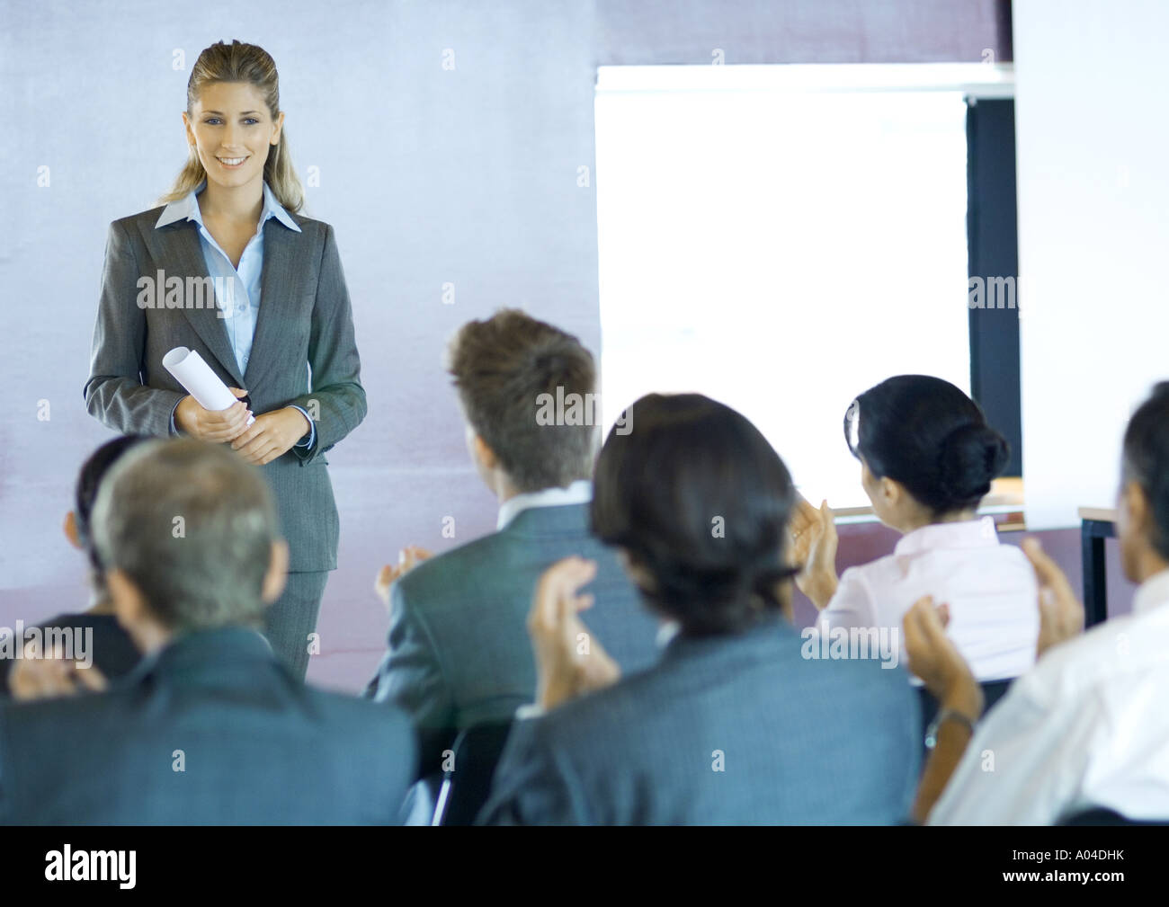 Executives sitting in seminar, woman standing facing group Stock Photo