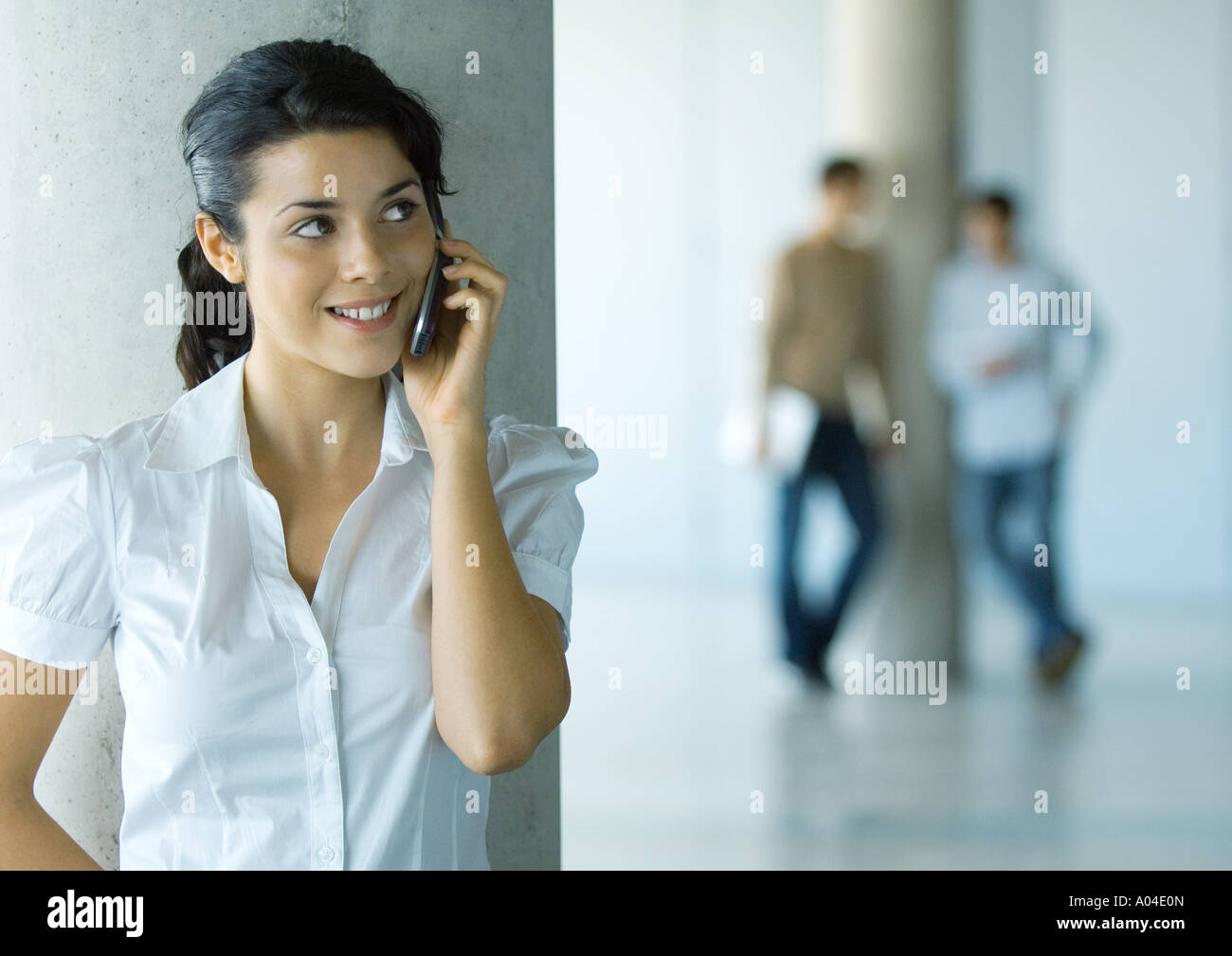 Young woman using cell phone, two men in background Stock Photo