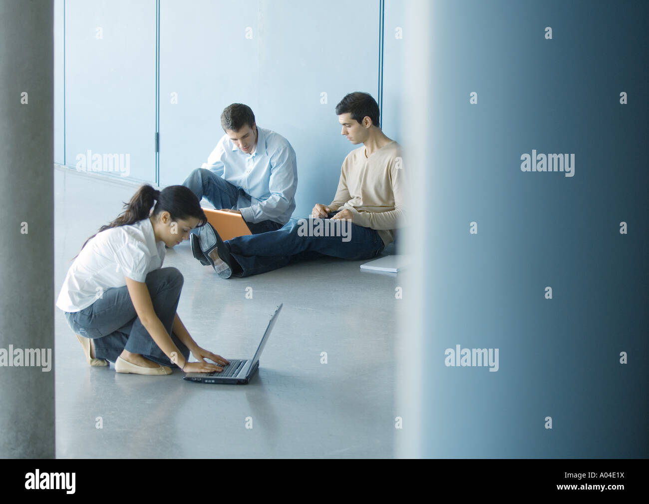 Young woman and two young men using laptops on floor Stock Photo