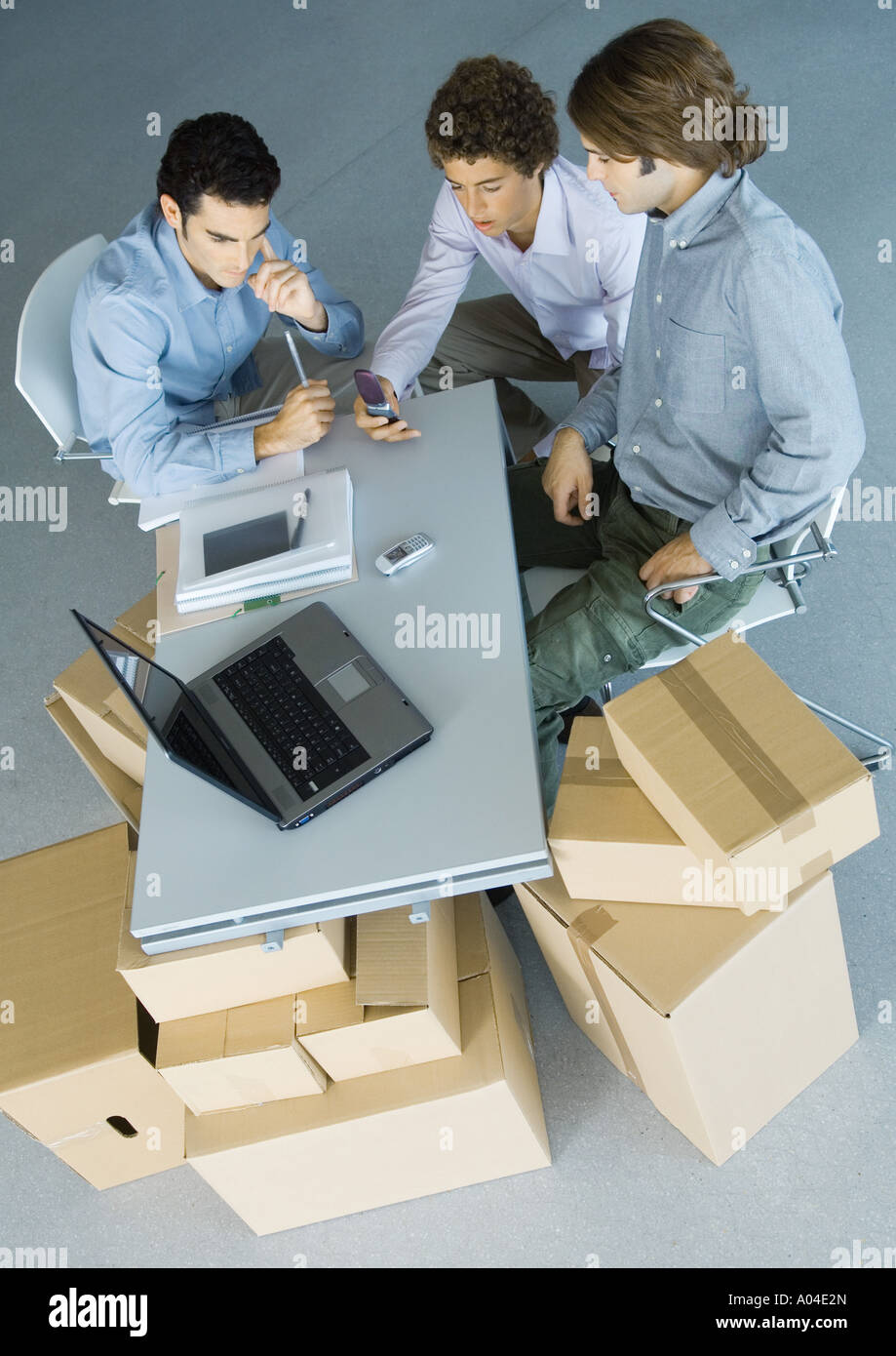 Businessmen sitting at table top supported by cardboard boxes, high