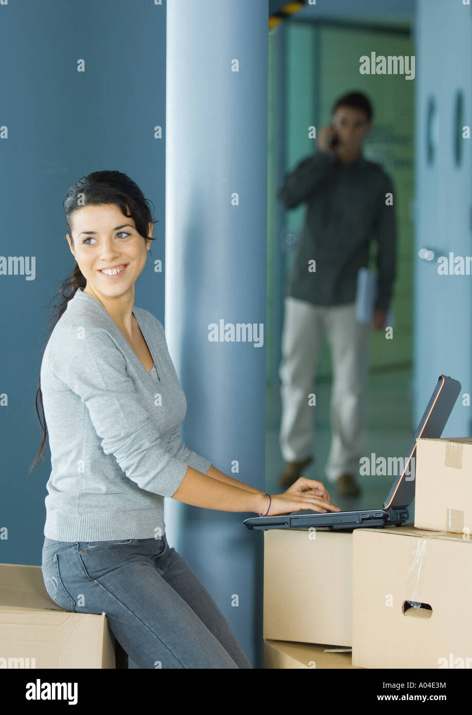 Young woman using laptop on cardboard box Stock Photo