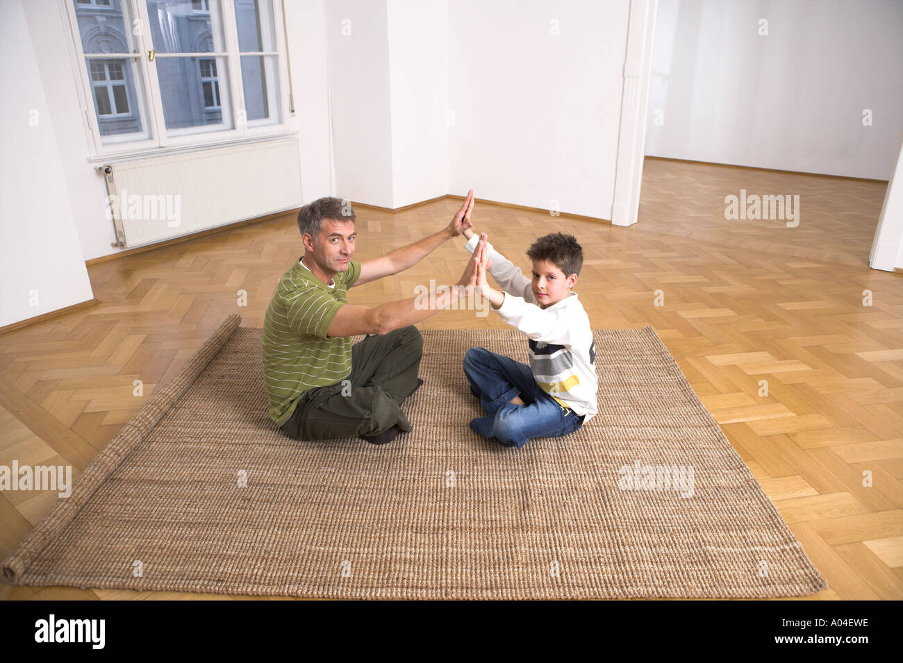 Father And Son Sitting On Carpet Clapping Hands Together In Empty