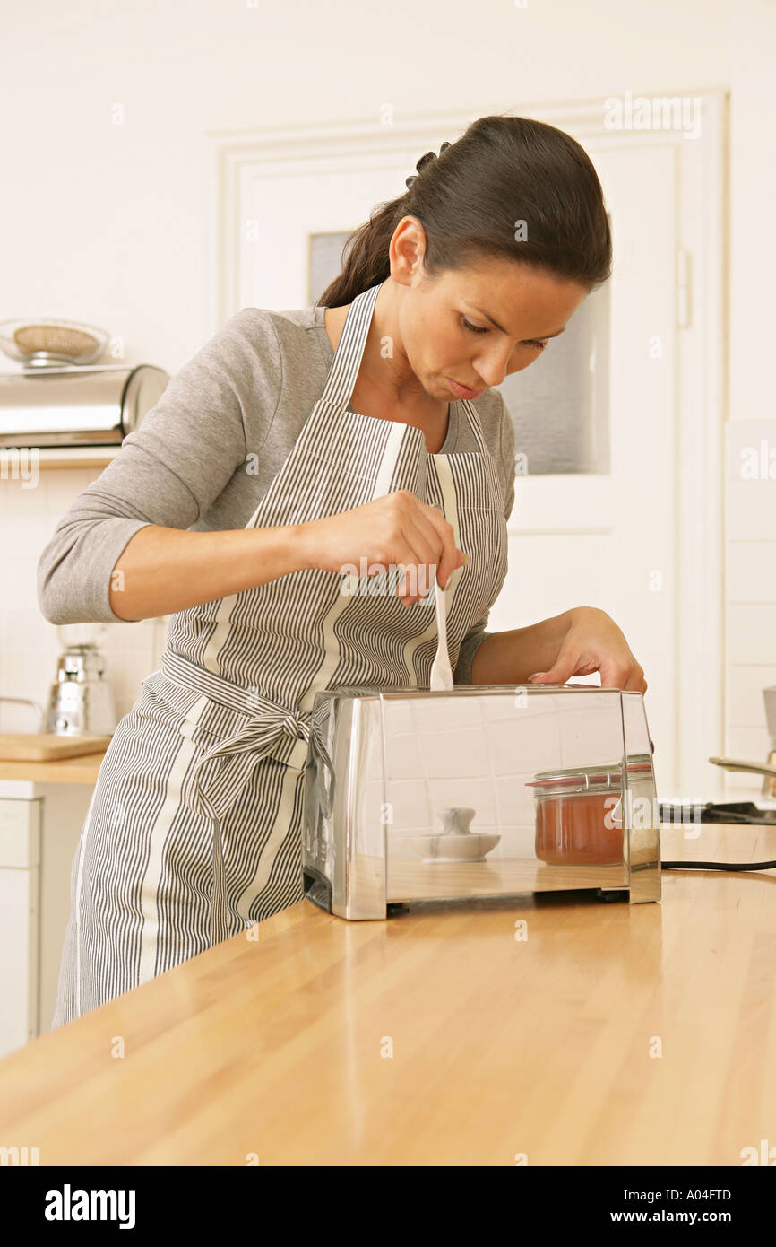 woman in apron in kitchen putting fork into toaster Stock Photo Alamy