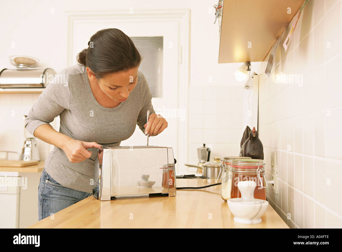 woman in kitchen sticking fork into silver toaster Stock Photo Alamy