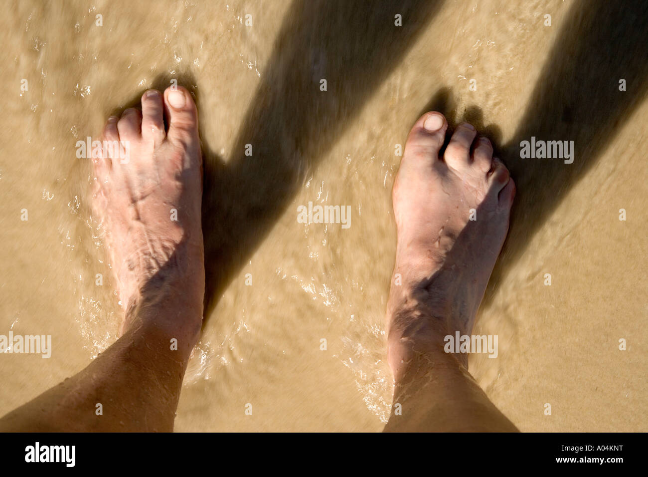 Barefoot on beach, receding tide, reflective shadows. Stock Photo