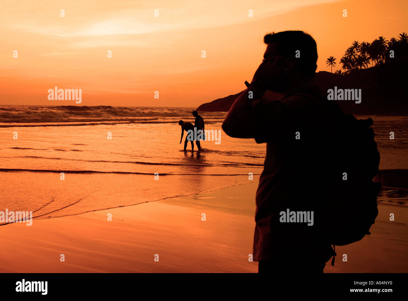 A tourist talking over his mobile phone in the backdrop of a sunset at Kovalam in Kerala Stock Photo