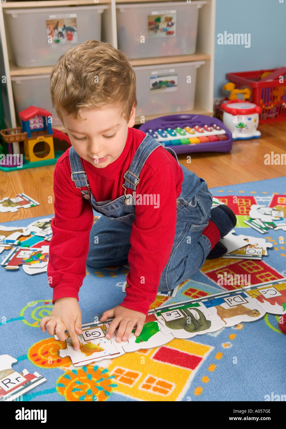 3 yr old boy puts in piece of alphabet puzzle on rug in his room Stock Photo