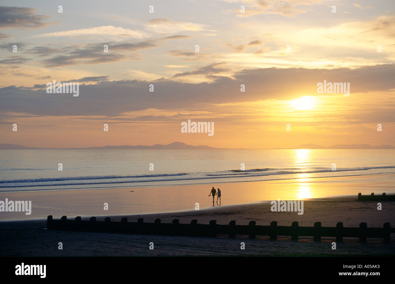 Sunset over the beach at the holiday seaside resort town of Barmouth in Gwynedd west Wales, UK.  Young couple strolling on beach Stock Photo
