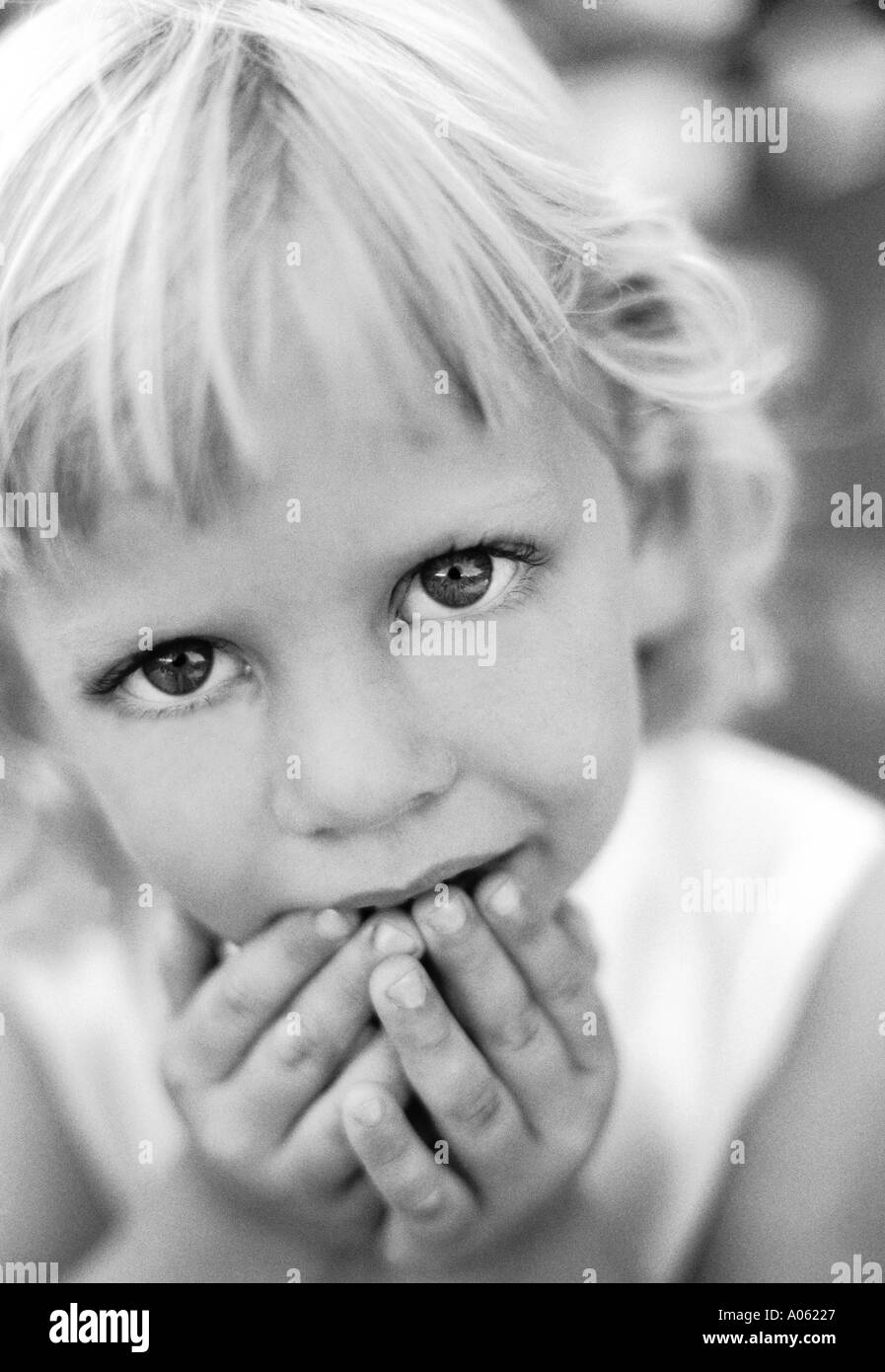 Close up face portrait of young little girl 5,6,7 old looking at camera with innocent big sweet sad eyes and hands at lips mouth Stock Photo