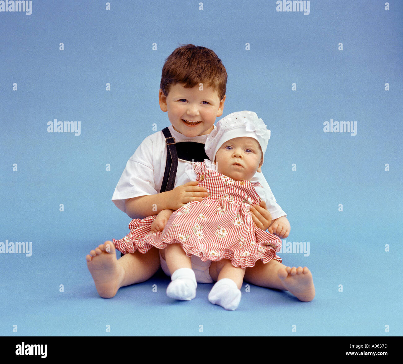 children child little boy in bavarian dress is holding his little sister a baby studio photo blue background Stock Photo