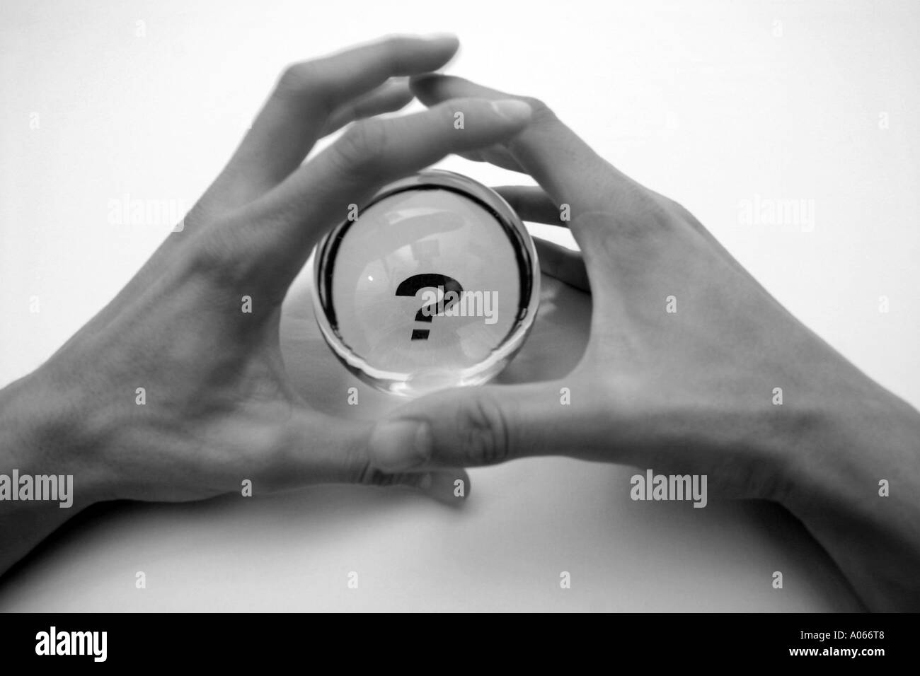 Two hands of a person seen near a circular glass having a question mark on it Stock Photo