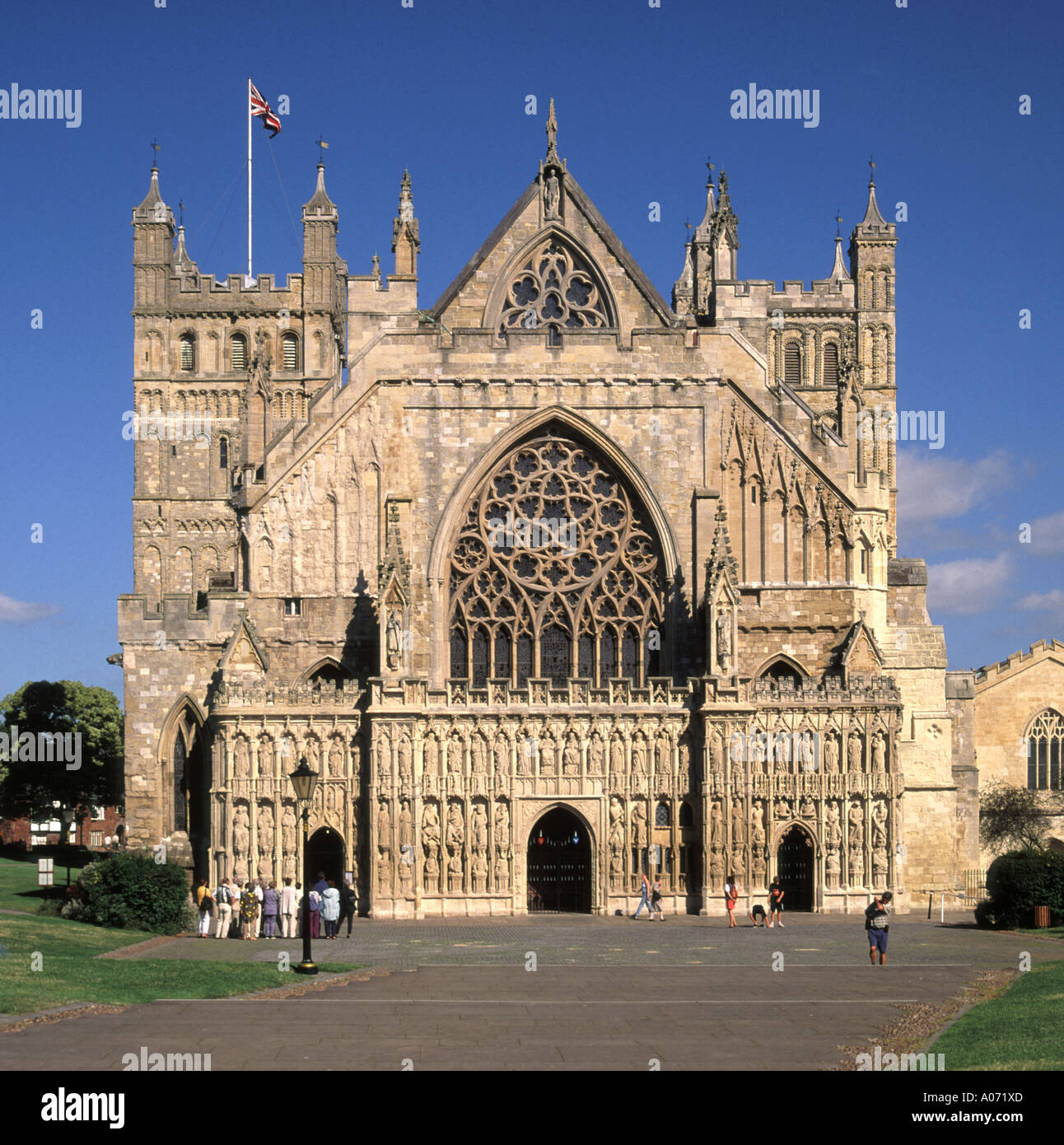 Union flag above Norman Gothic architecture of the West Front & towers of historical Anglican Exeter Cathedral building in Cathedral Square Devon UK Stock Photo