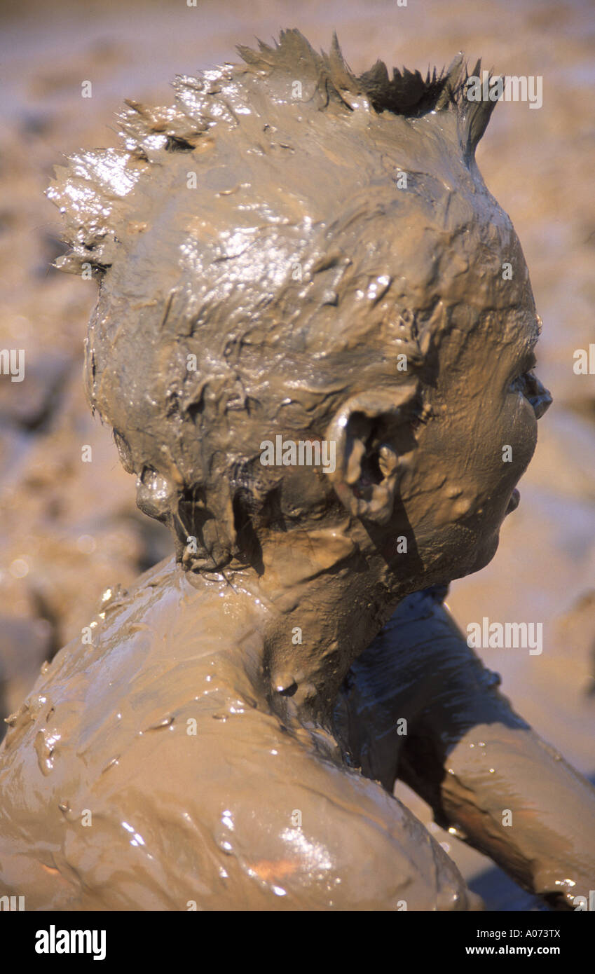 Child playing in thick mud with head and body covered by brown mud