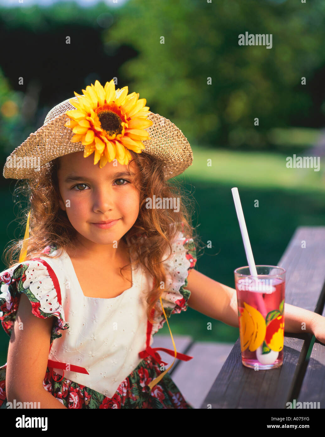 Young Girl Sitting in Garden with Soft Drink and Wearing Straw Hat with Sunflower UK Stock Photo