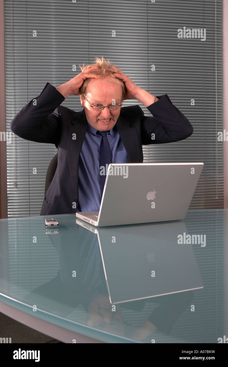 Businessman using a laptop computer looking stressed and holding his ...