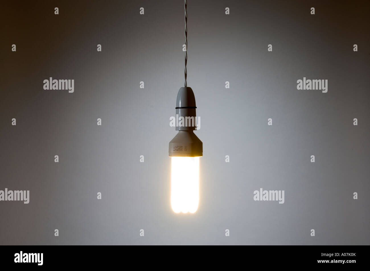 A fluorescent, energy-saving light bulb hanging by a twisted flex wire Stock Photo