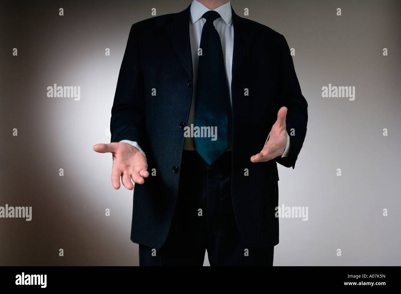 A man in a dark grey business suit gesturing with his hands as if making a point during a presentation Stock Photo