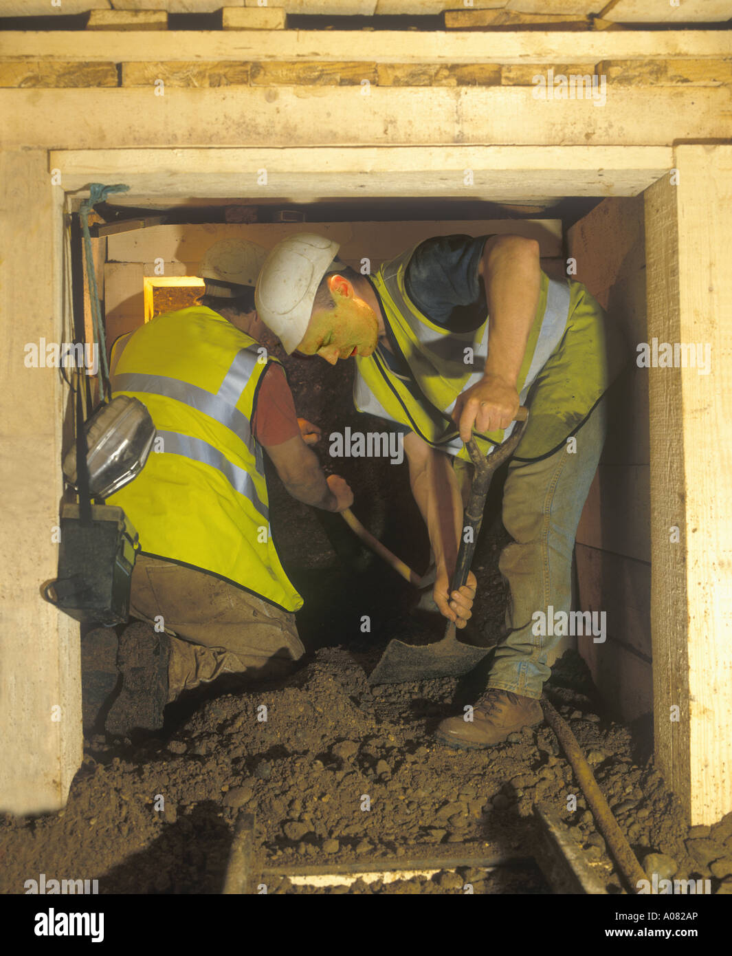 workmen digging underground in a tunnel including a railway system with wooden supports Stock