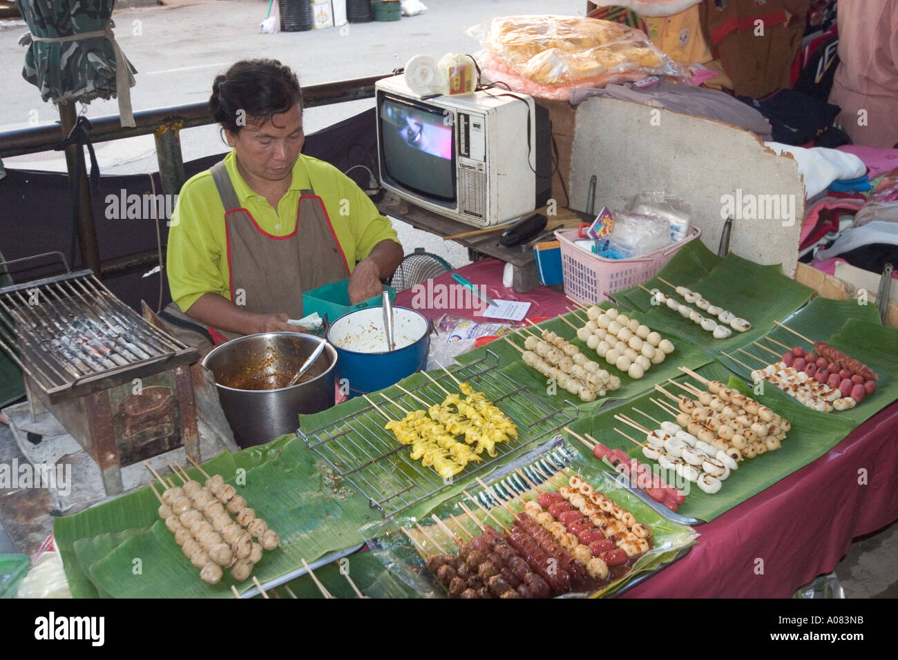 Lady vendor ar Street stall selling cooked meat and fish balls with TV on in background Stock Photo