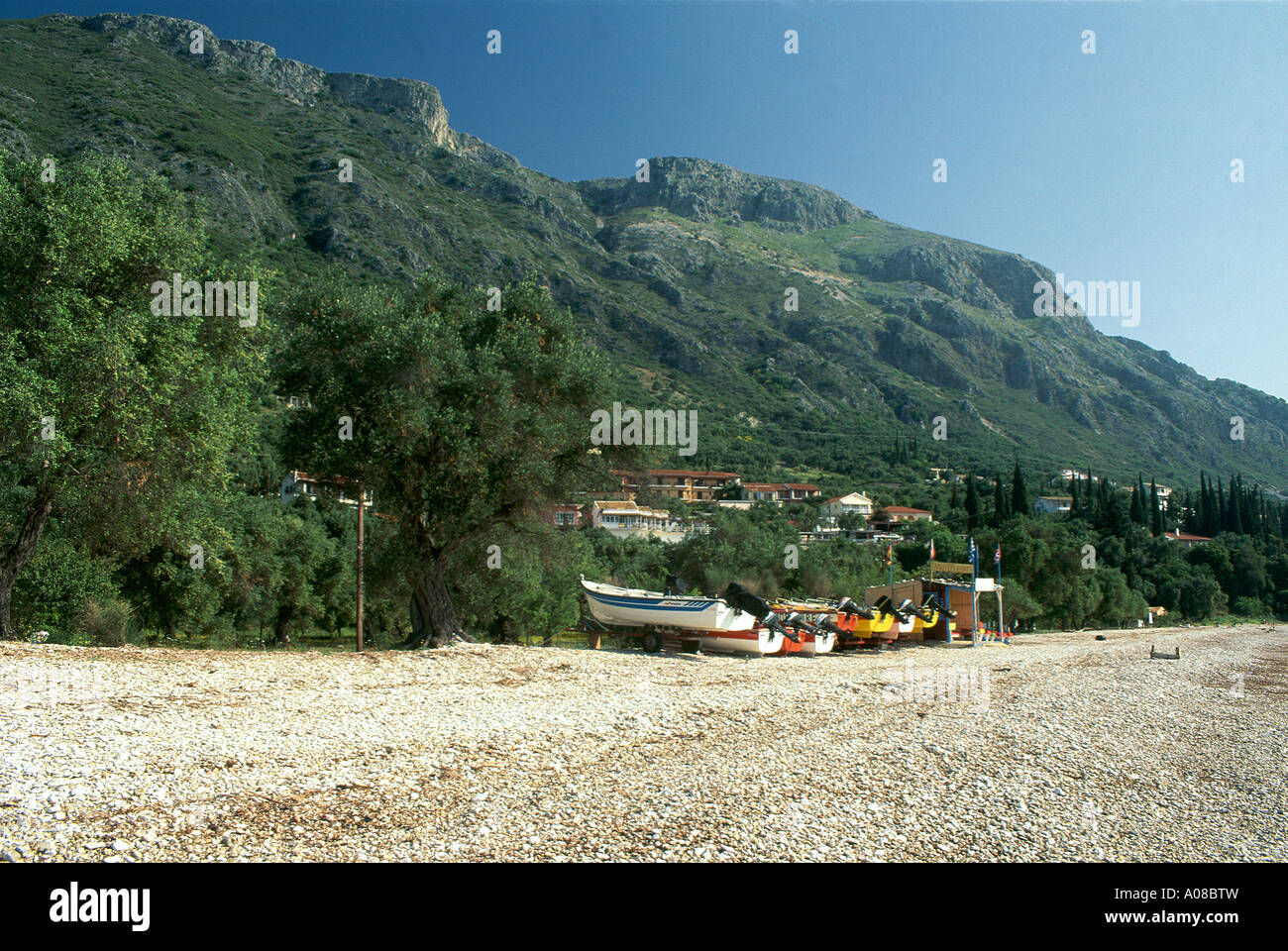 Small boats pulled well up the shingle beach beneath the scattered dwellings of the resort of Barbati situated to the north of Corfu Town on the east coast of the island Stock Photo