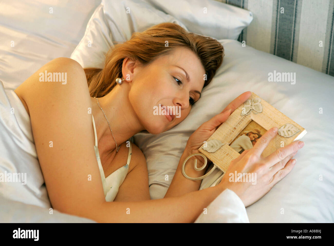 Frau liegt mit Foto im Bett und denkt an ihren Liebsten, woman lying in bed and thinking of her sweetheart Stock Photo