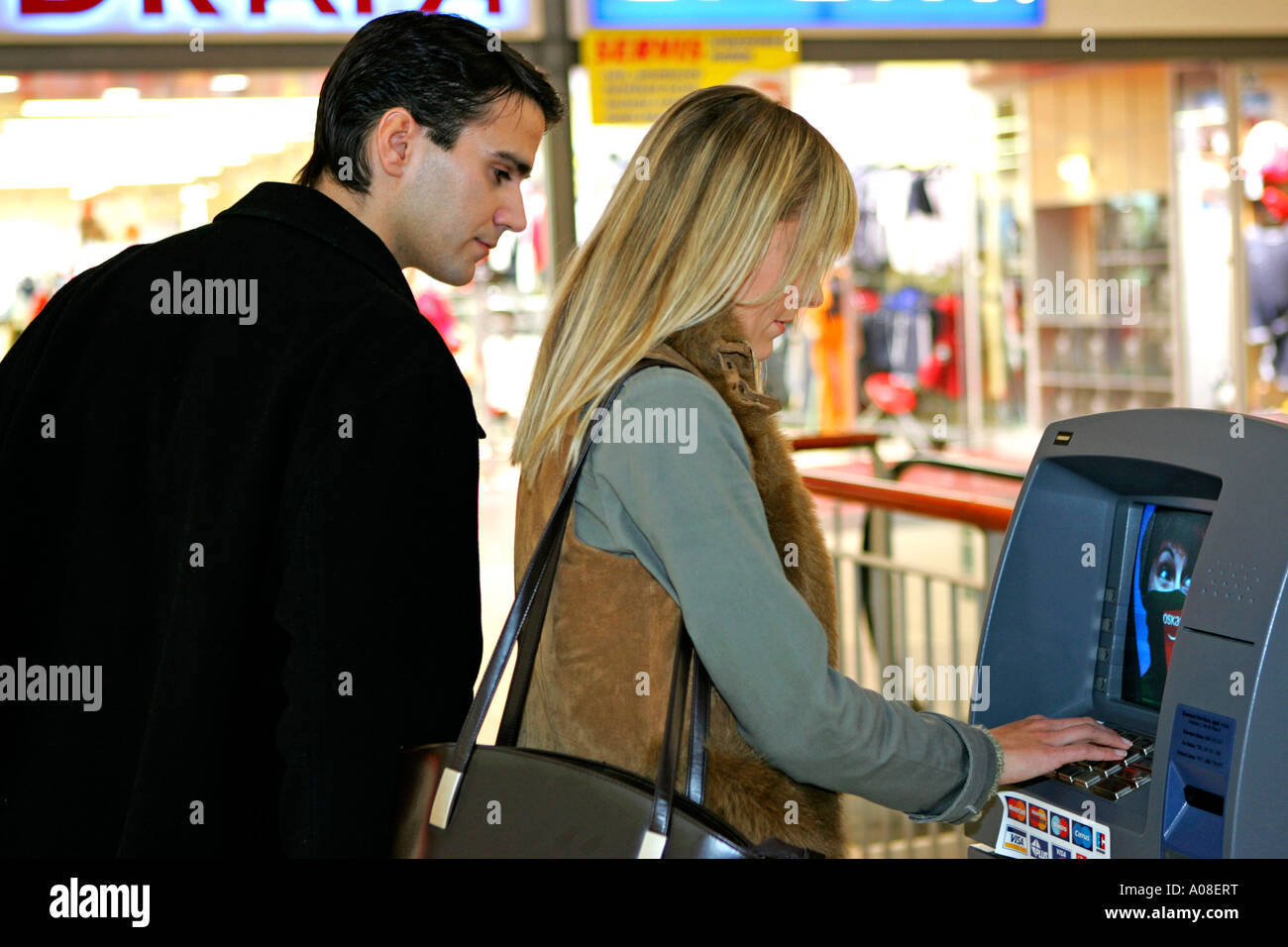 Frau am Geldautomaten Mann schaut nach PIN Nummer, woman at cash dispenser man looking for pin code Stock Photo