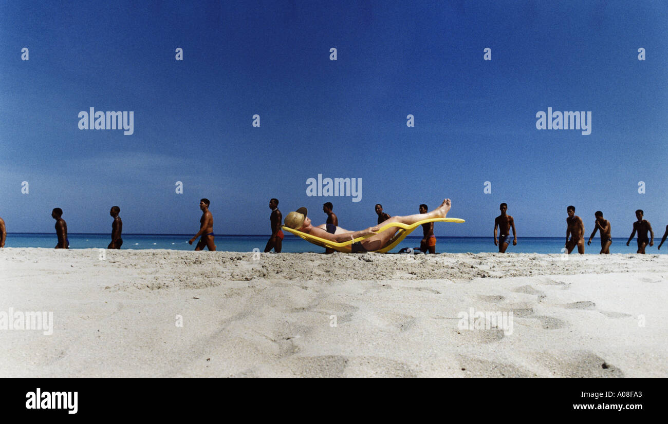 woman sunbathing on beach while twelve men pass by Stock Photo