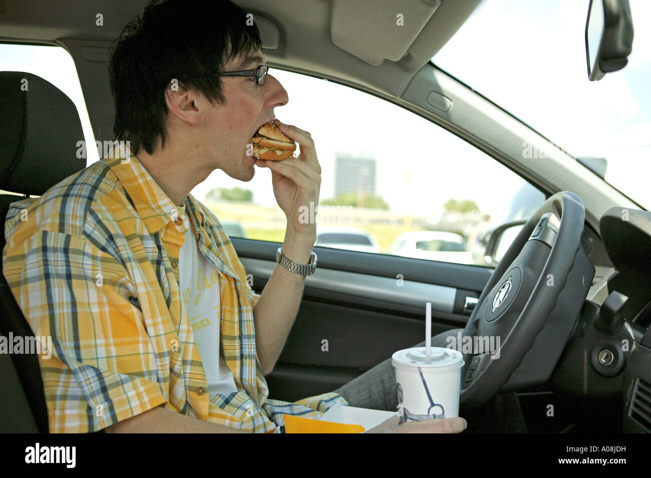 Junger Mann isst einen Hamburger im Auto, Man having a snack in car Stock Photo