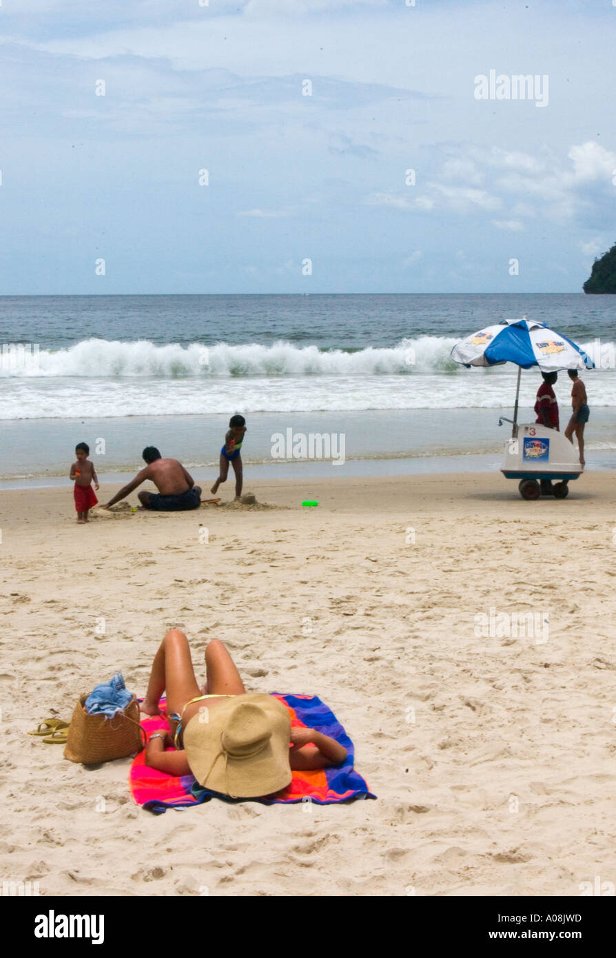 young woman sleeps on the beach, covering her face with a giant straw hat on Maracas beach in Trinindad in the Caribbean Stock Photo