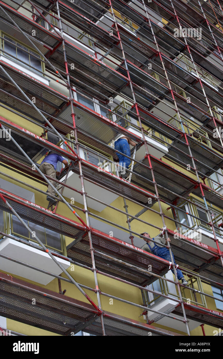 Three workmen climbing up ladders on scaffolding outside a block of