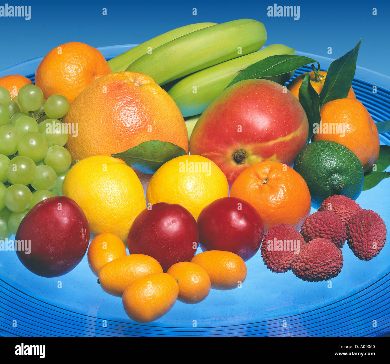 different fruits on blue flat banana grapes lychees kumquat mango lemon grapefruit plum mandarin bowl blue light transparent Stock Photo