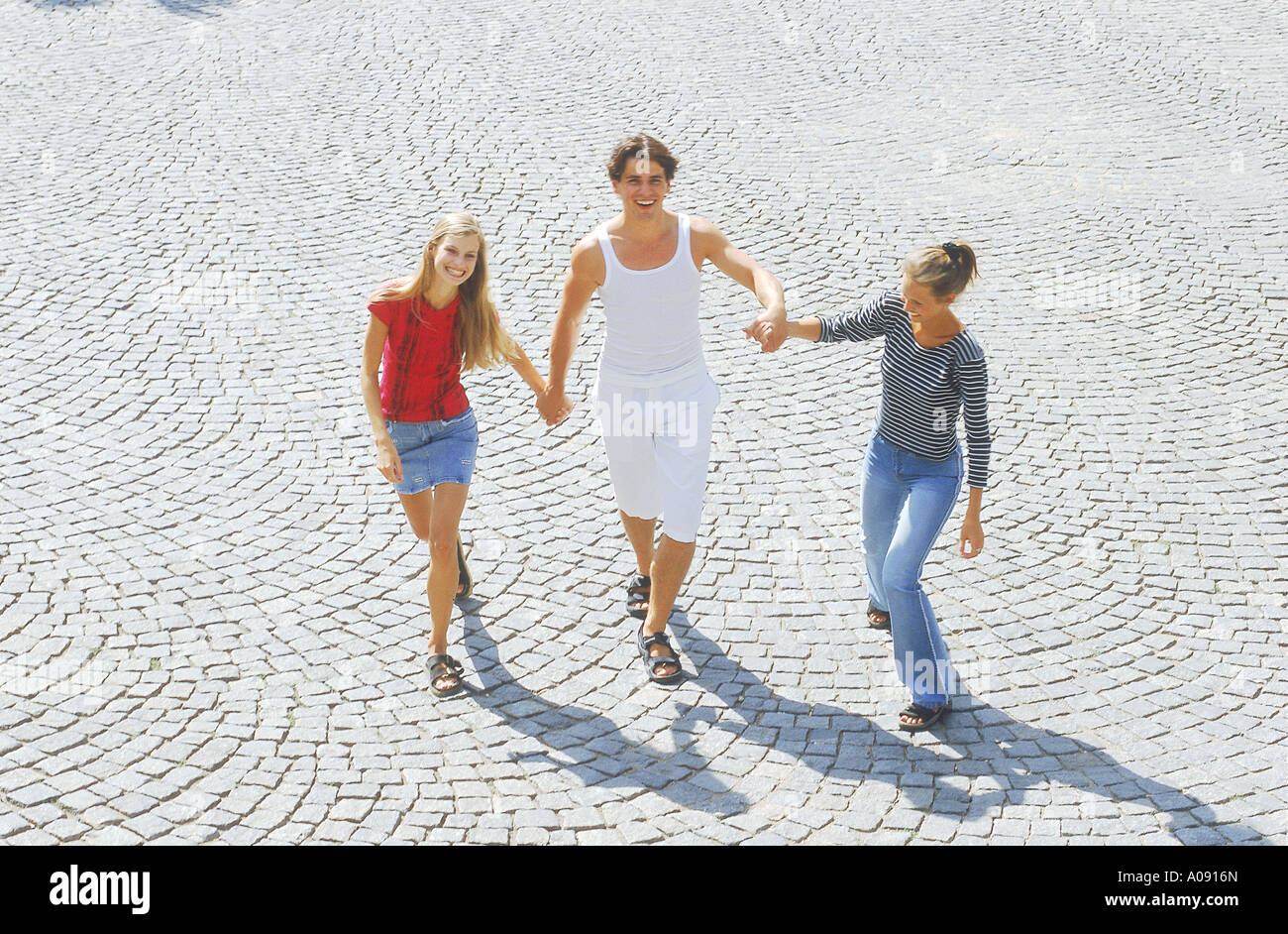 Portrait of a young man and two young women walking holding hands Stock ...