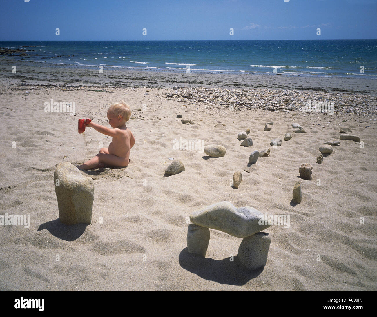 Young boy playing on the white sandy beach at Carnac with pretend megaliths Stock Photo