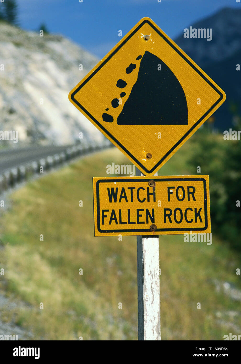 WATCH FOR FALLEN ROCK warning sign with road and rocky cliff in