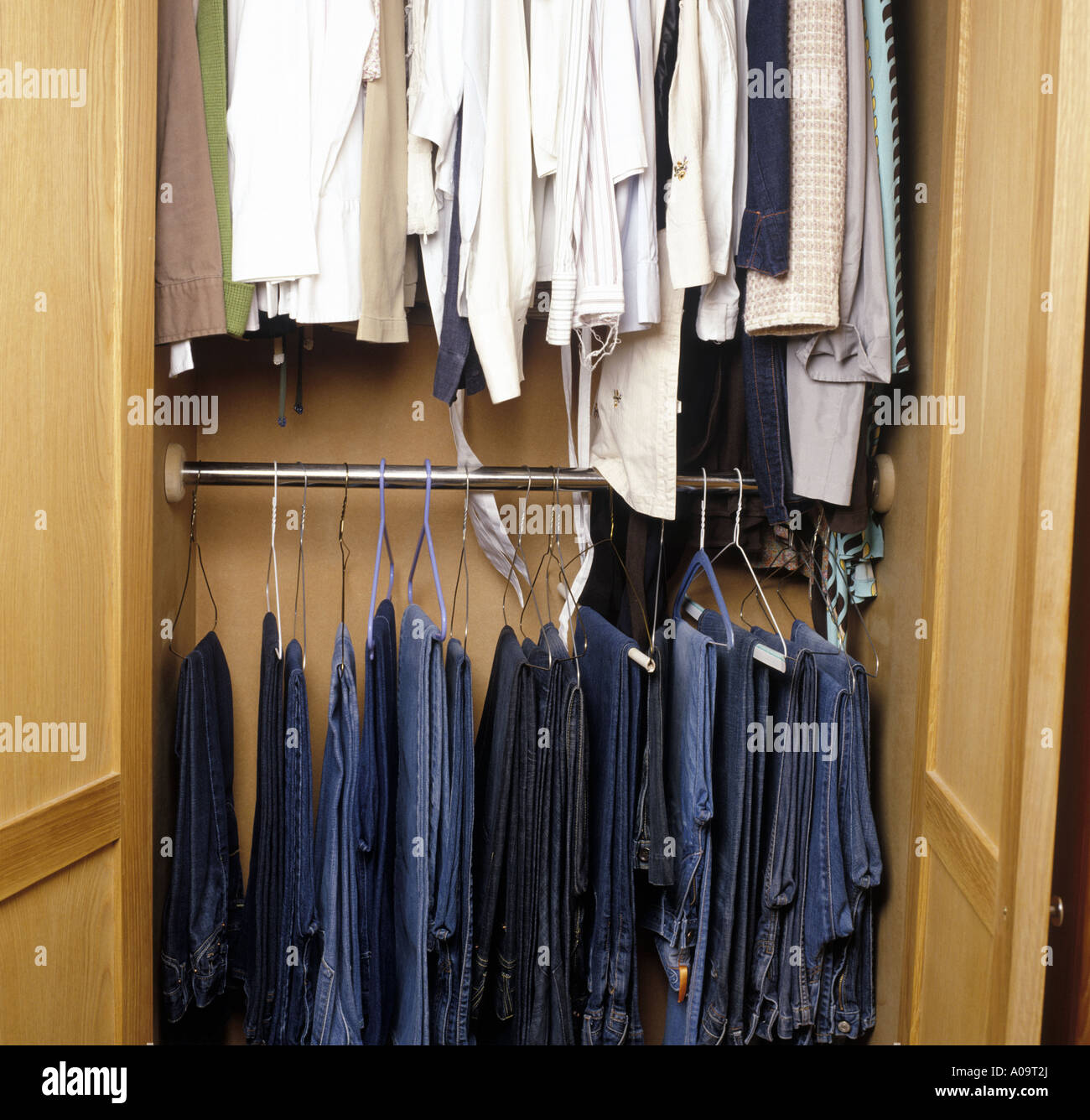 a selection of jeans and shirts hanging up in a wardrobe Stock Photo