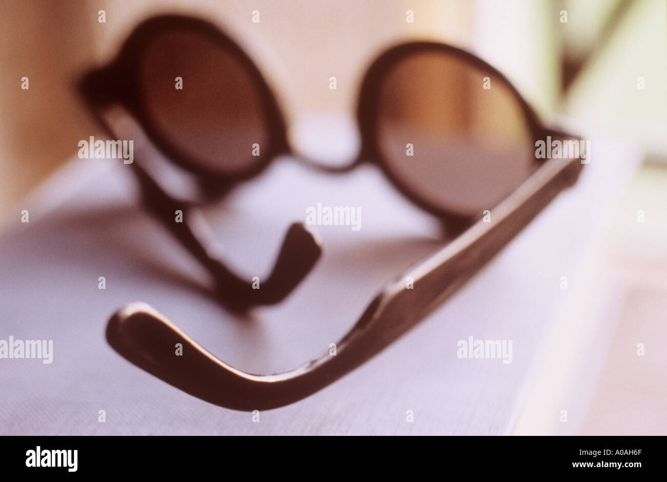 A pair of sunglasses with circular lenses lying on a book by a window Stock Photo