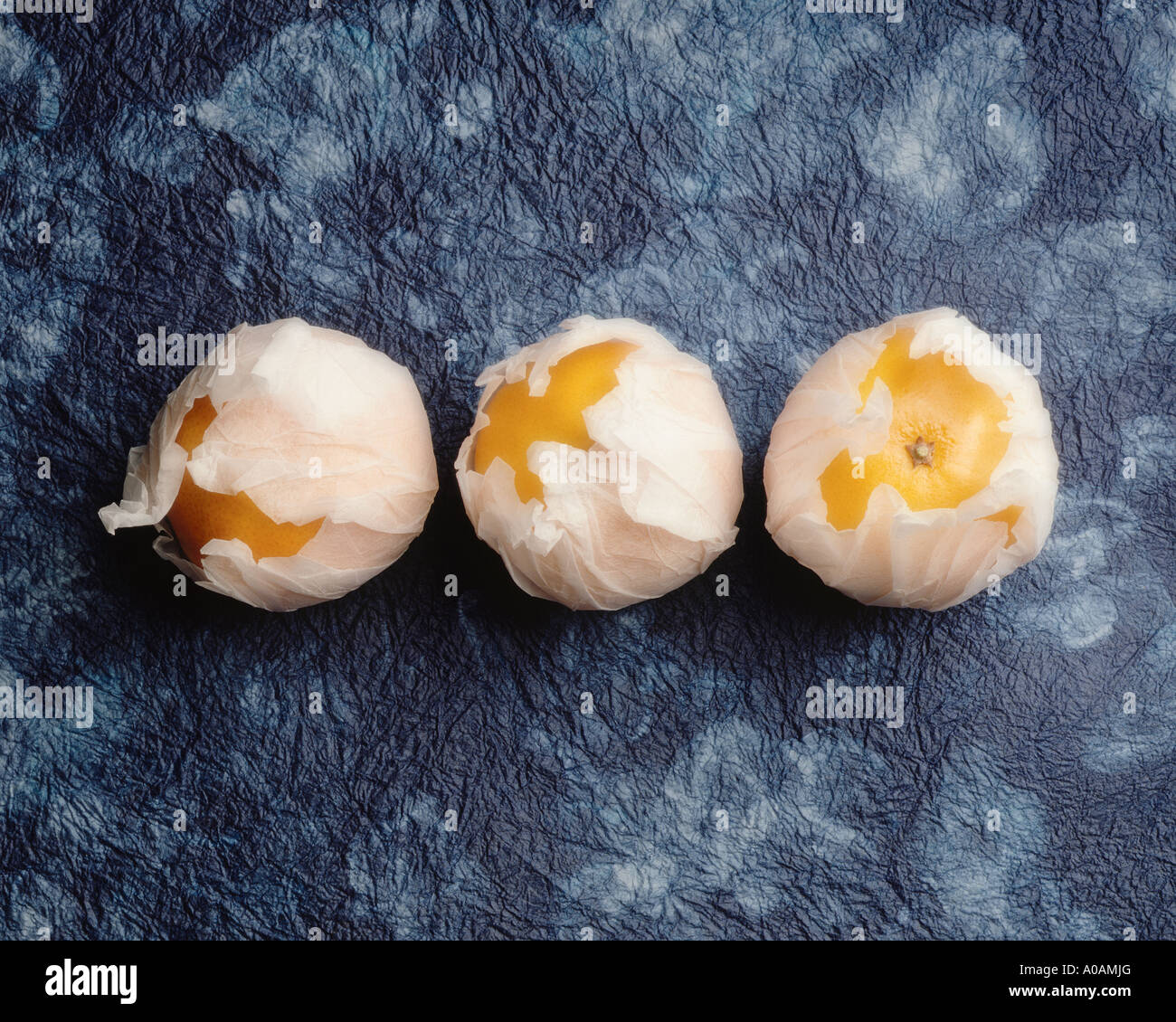 Three mandarin oranges wrapped in tissue paper with handmade paper