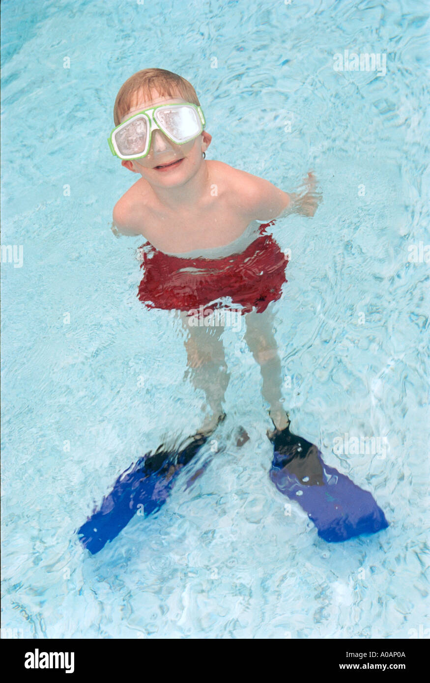 A vertical color image of a blonde boy in a pool wearing fogged swim goggles red swim trunks and big blue flippers Stock Photo